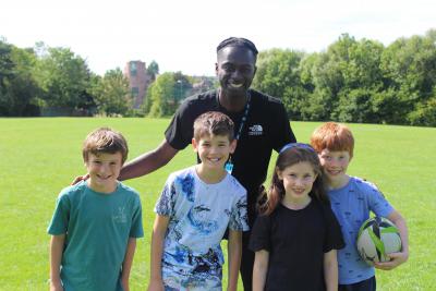 four children in sports gear standing with staff member on a field