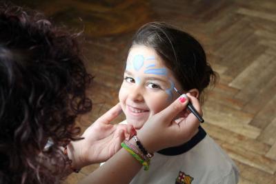 girl smiles as she has her face paint done by staff member