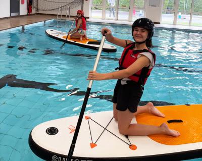 Two children paddleboarding in a swimming pool at XUK summer camp