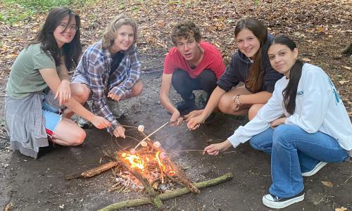 group of teenagers roasting marshmallows around a fire at summer camp