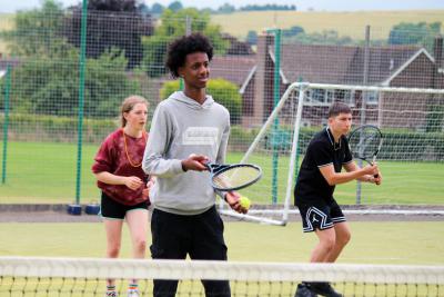 Three teenagers playing tennis at UK summer camp