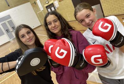 three teenage girls holding up boxing gloves at summer camp