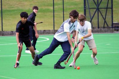 group of teenage boys and an XUK staff member playing hockey at summer camp