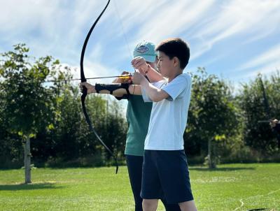 instructor helping child with archery bow and arrow at Sports Summer Camp - XUK Camps