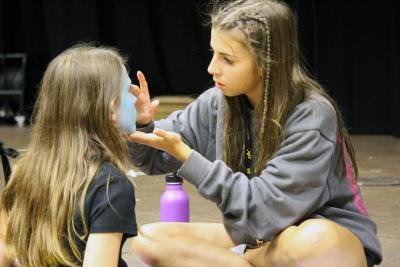 teenage girl completing leader in training at XUK camps helps young girl with facepaint