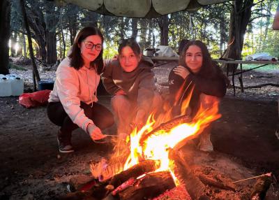 Three teenagers roasting marshmallows around a campfire at uk summer camps